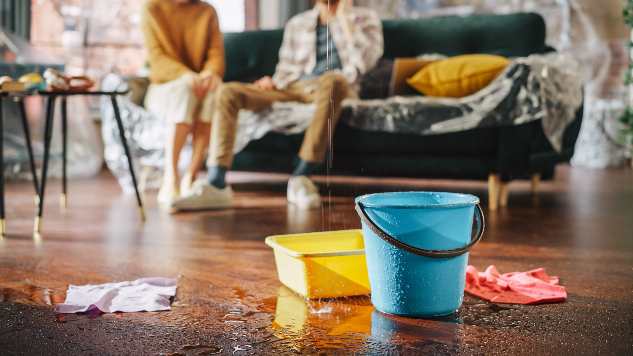 Water leak falling into a bucket in front of couple calling insurance