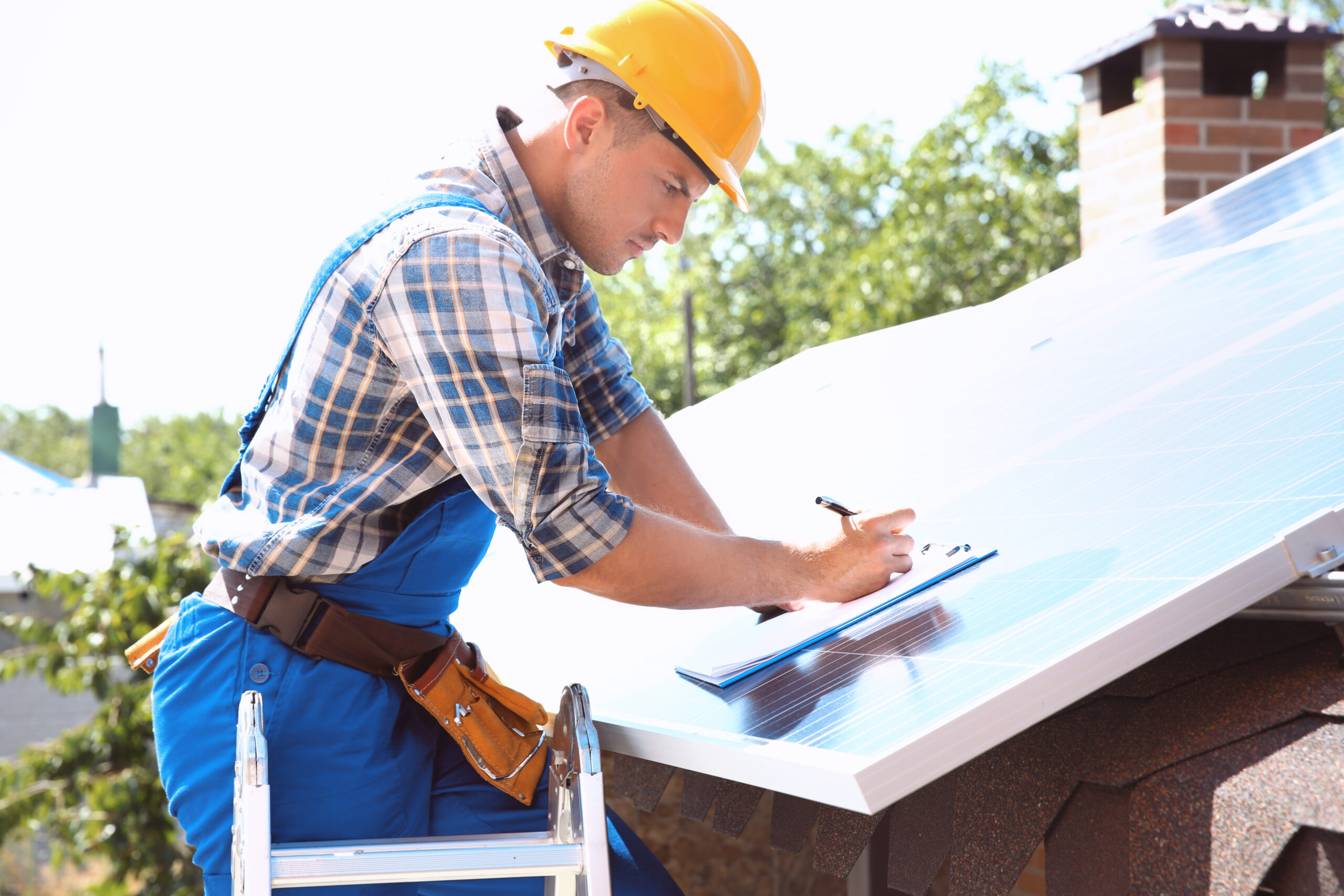 Roofer inspecting damage on a residential roof and taking notes