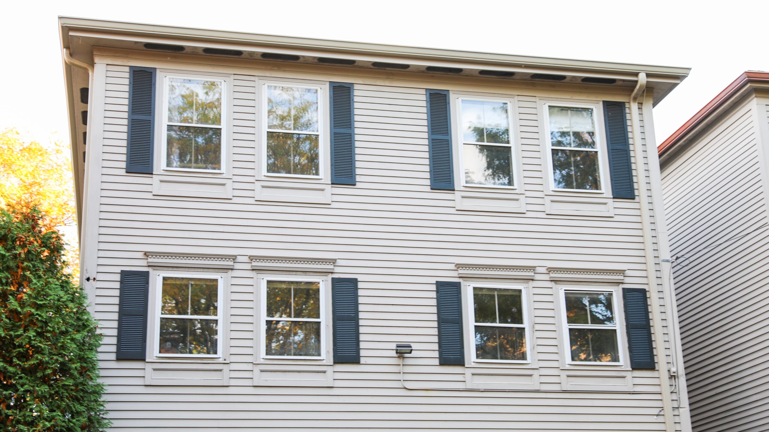 Large two-story home with off-white siding and lots of windows with dark blue shutters