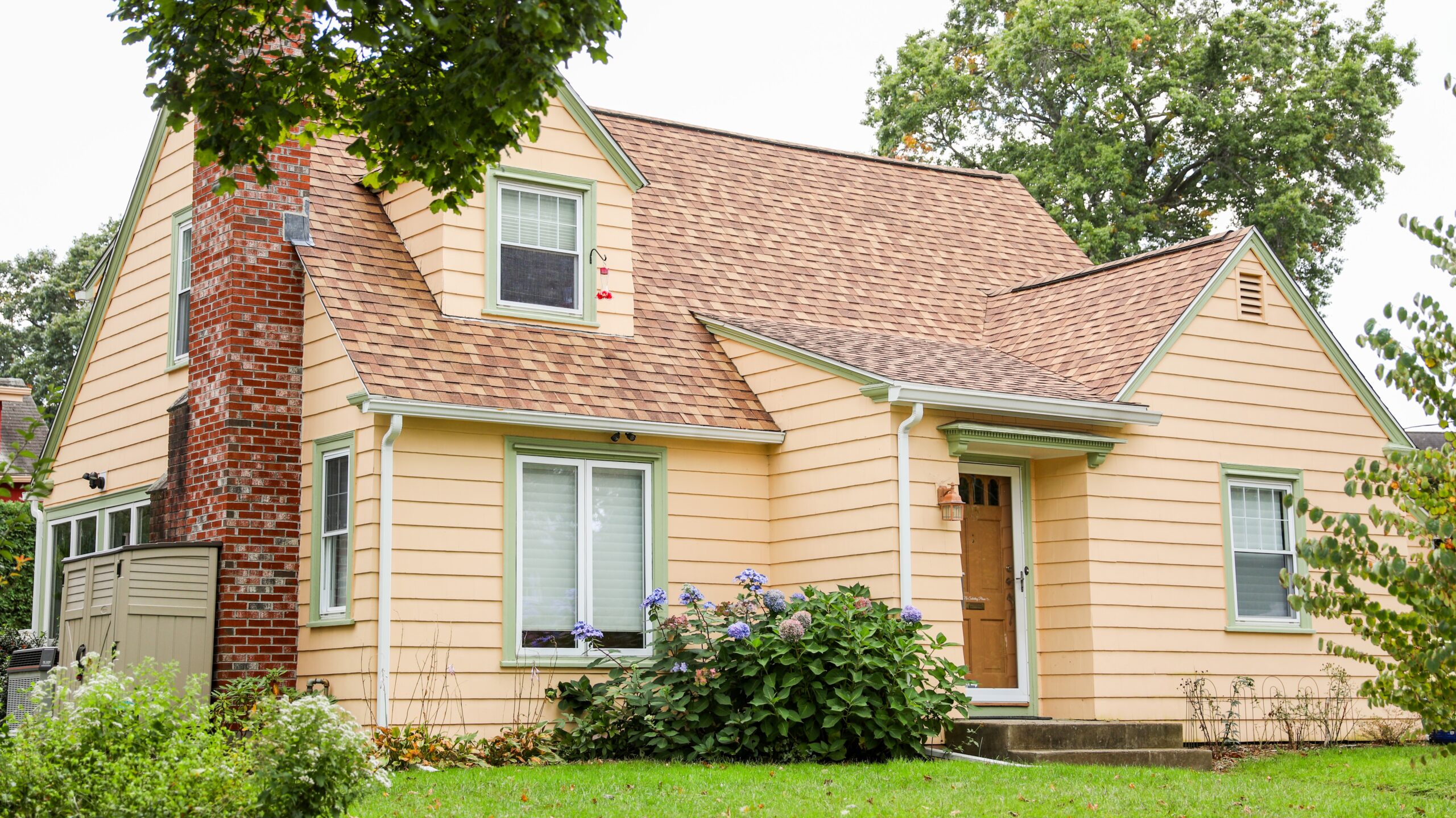 Home with yellow siding and brown asphalt shingle roof with a large brick chimney on the side