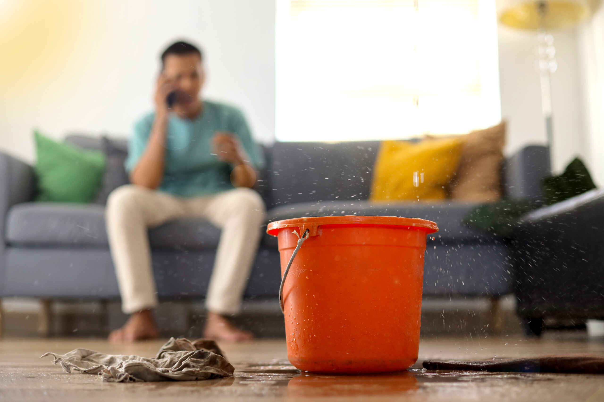 Red bucket with water falling from the roof in front of a man on the phone