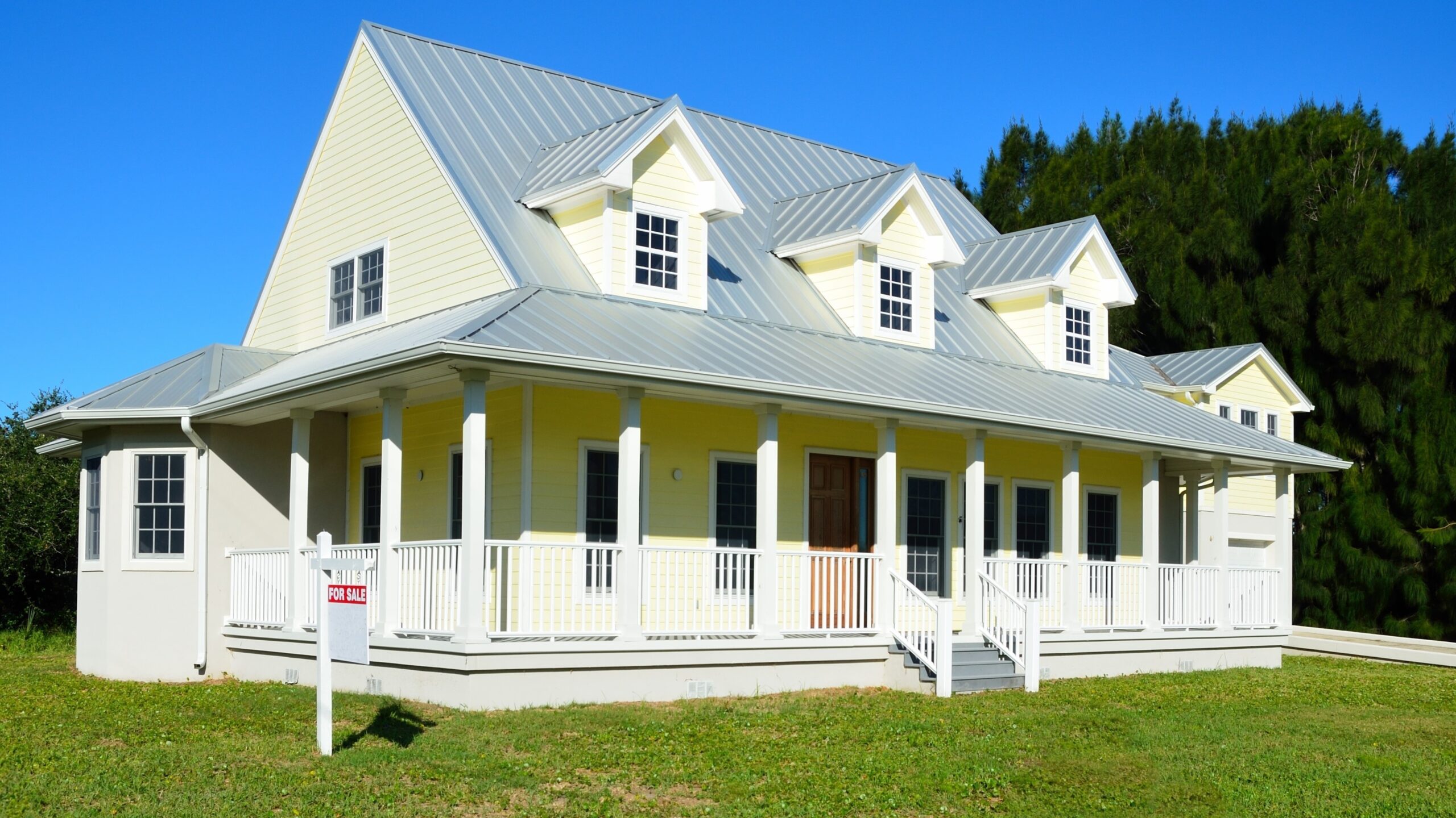 Home exterior with cream-colored siding and beautiful metal roof with a for sale sign out front