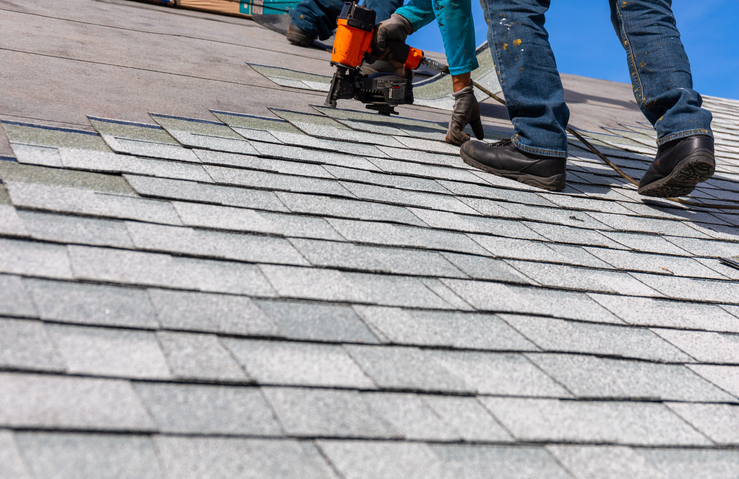 Roofer nailing asphalt shingles onto a roof