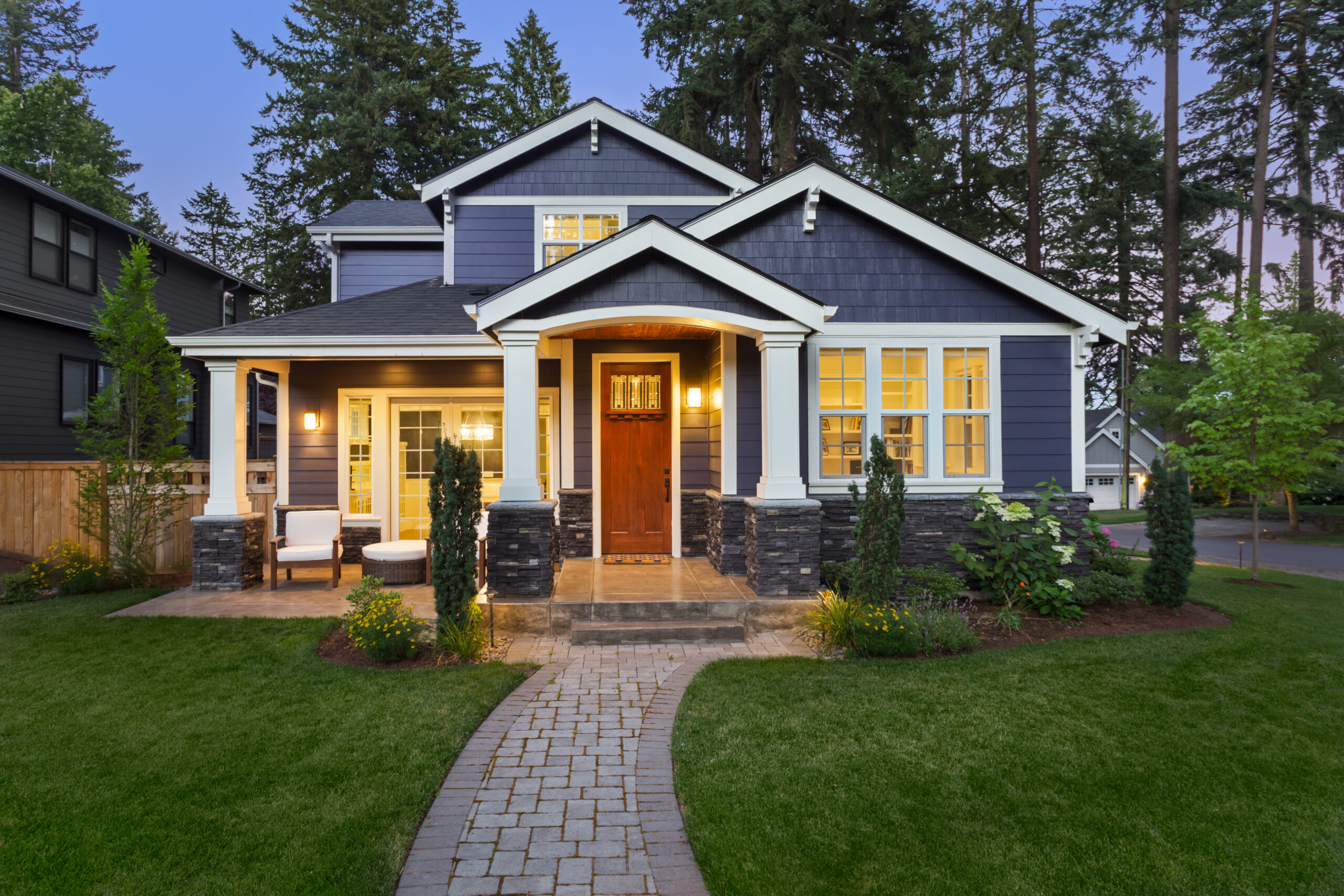 Blue house with a wood front door with lights on