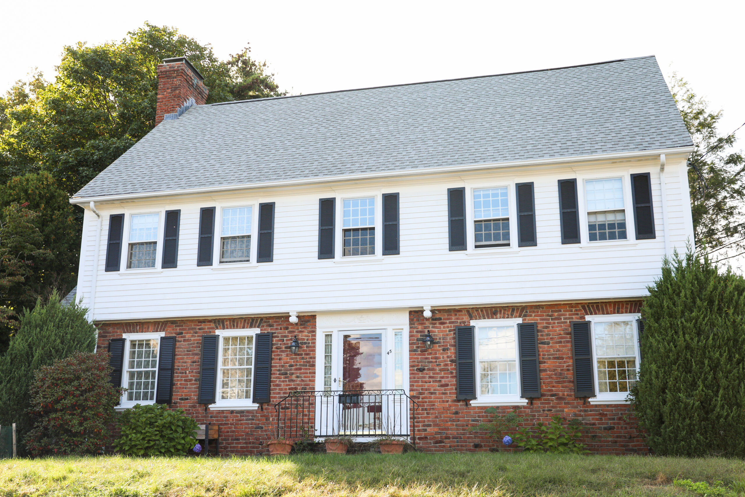 Two-story house with a large shingle roof, white siding on top half, and brick on bottom half