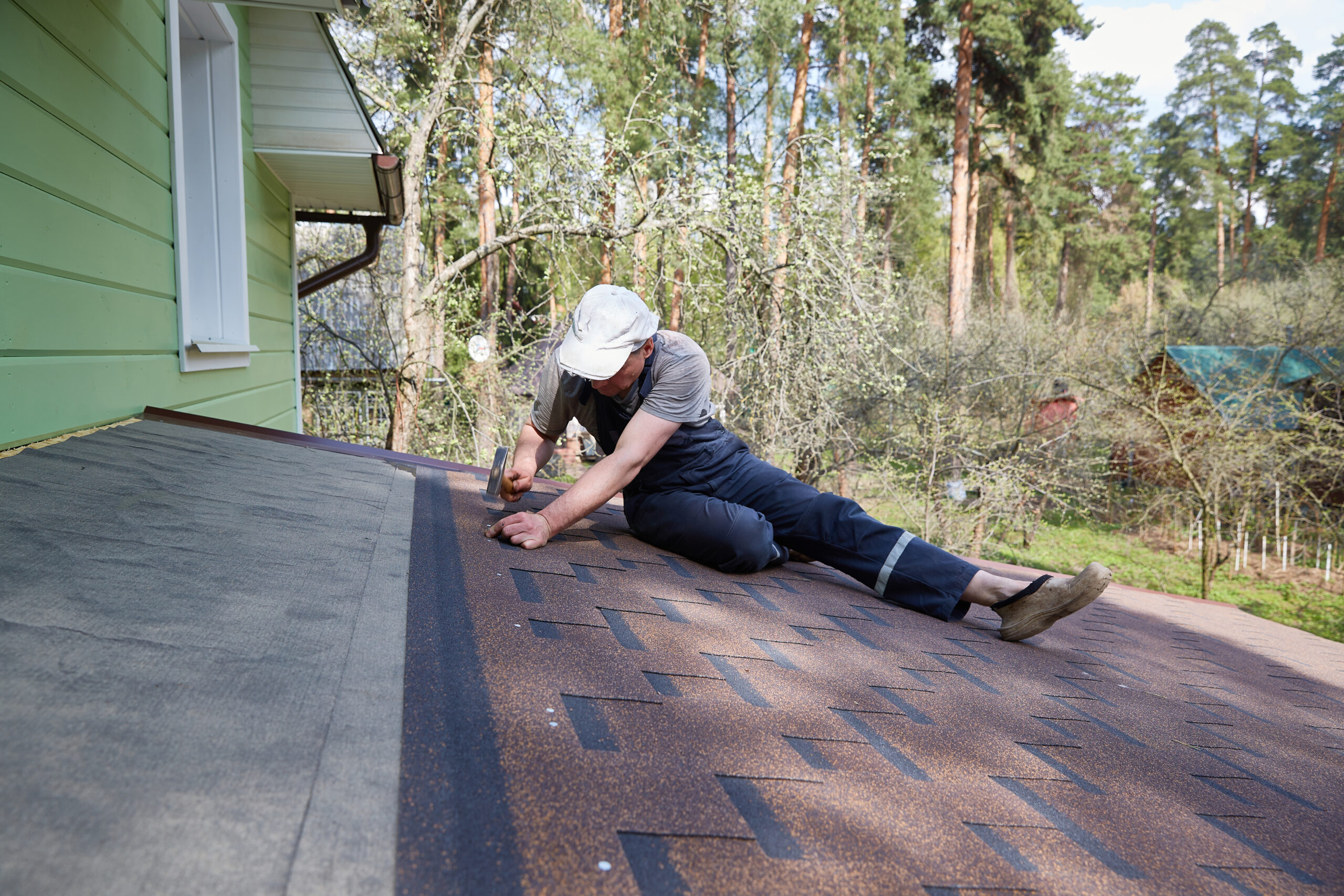 A roofer carefully works to repair the shingles on a roof.