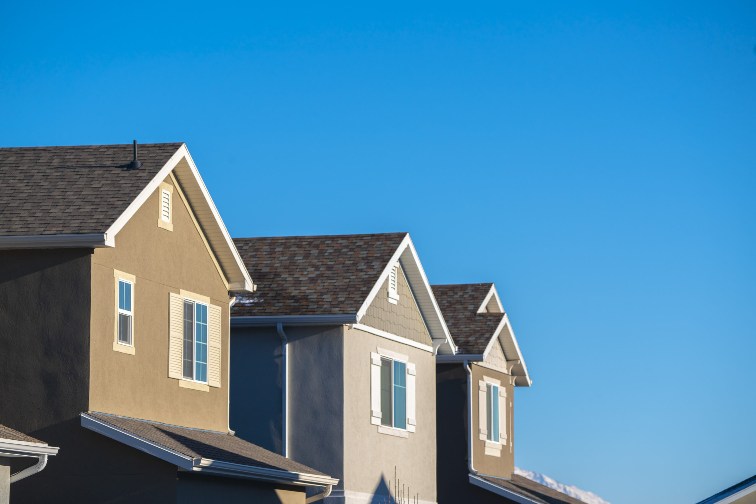 An angled shot of the top layer of three houses with stucco siding and asphalt shingle roofs.