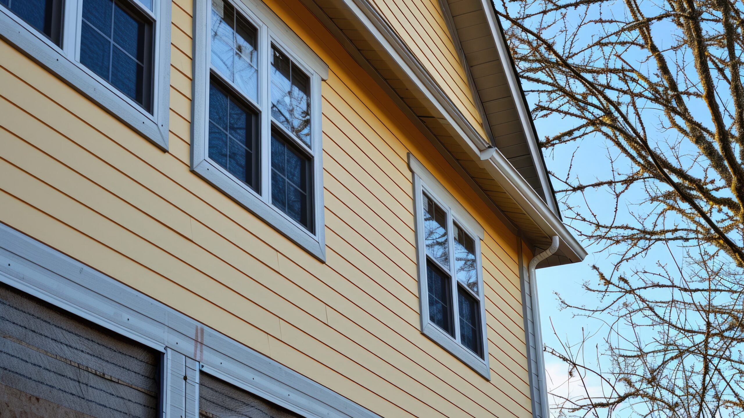 Home exterior with yellow siding and three beautiful windows with gray frames.