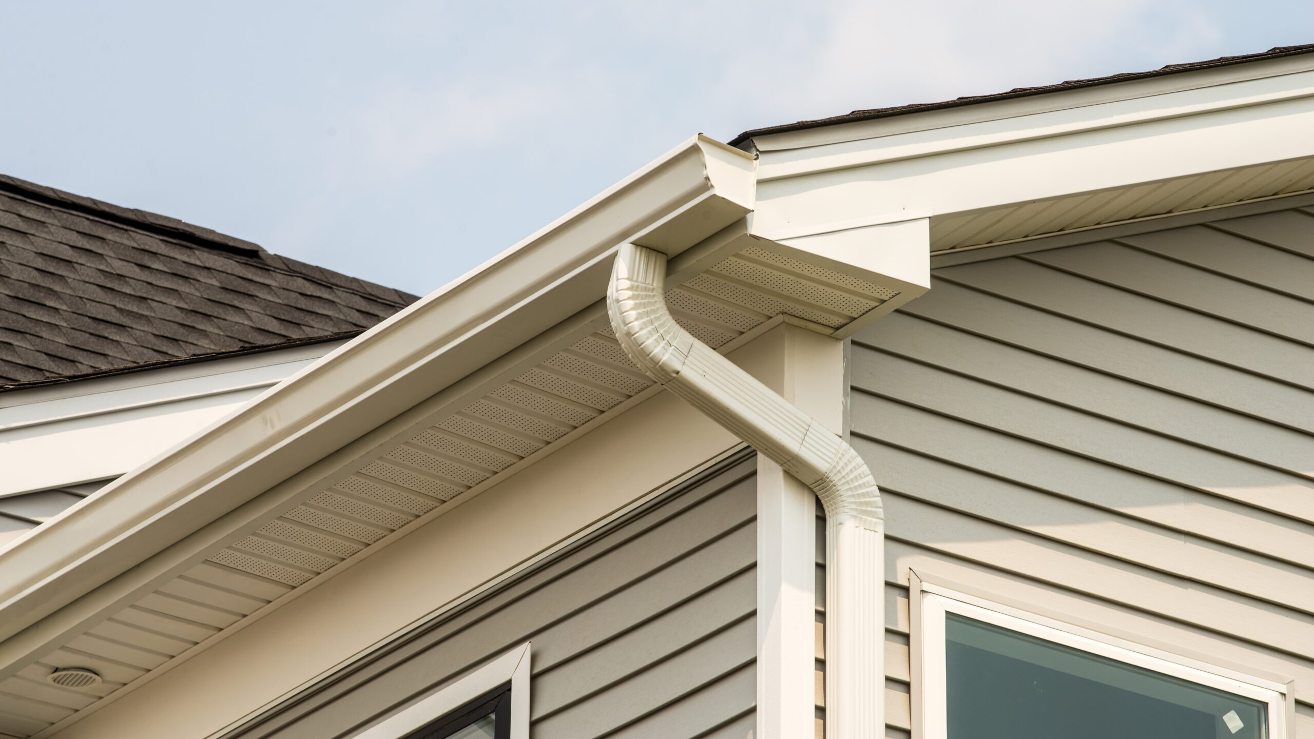 Exterior corner of a home with white siding and newly installed white seamless gutters.