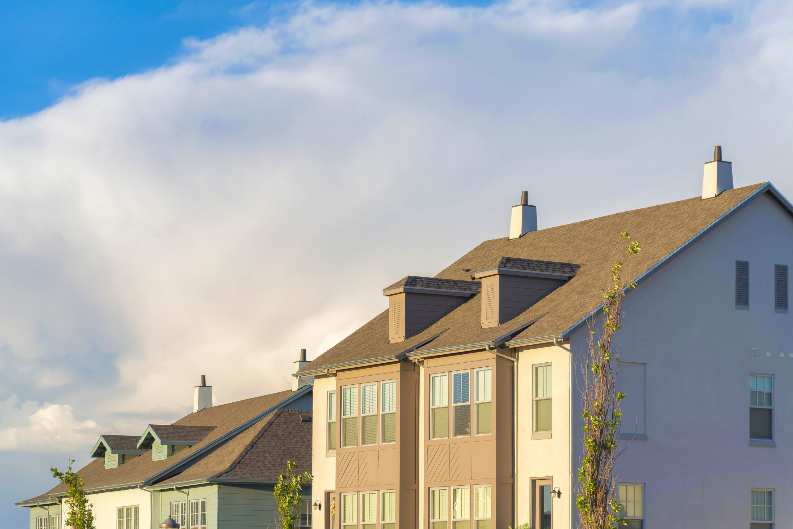An angled shot of the top layer of three houses with stucco siding and asphalt shingle roofs.
