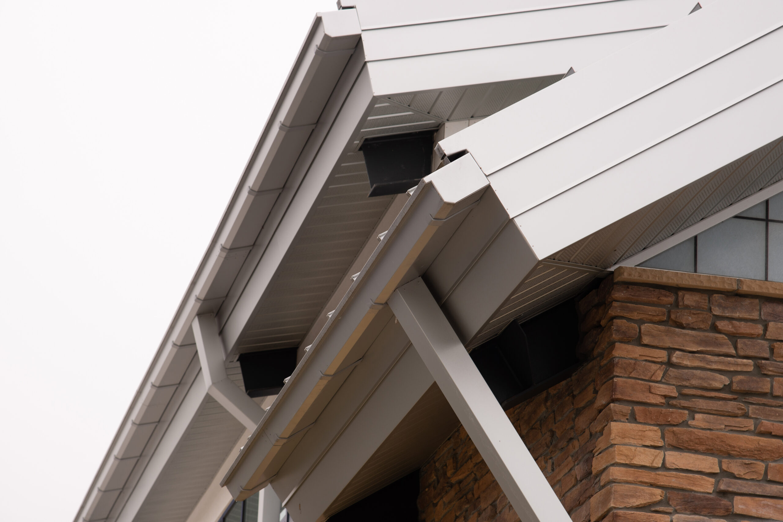 A closeup of new white seamless gutters on the edge of a brick house.