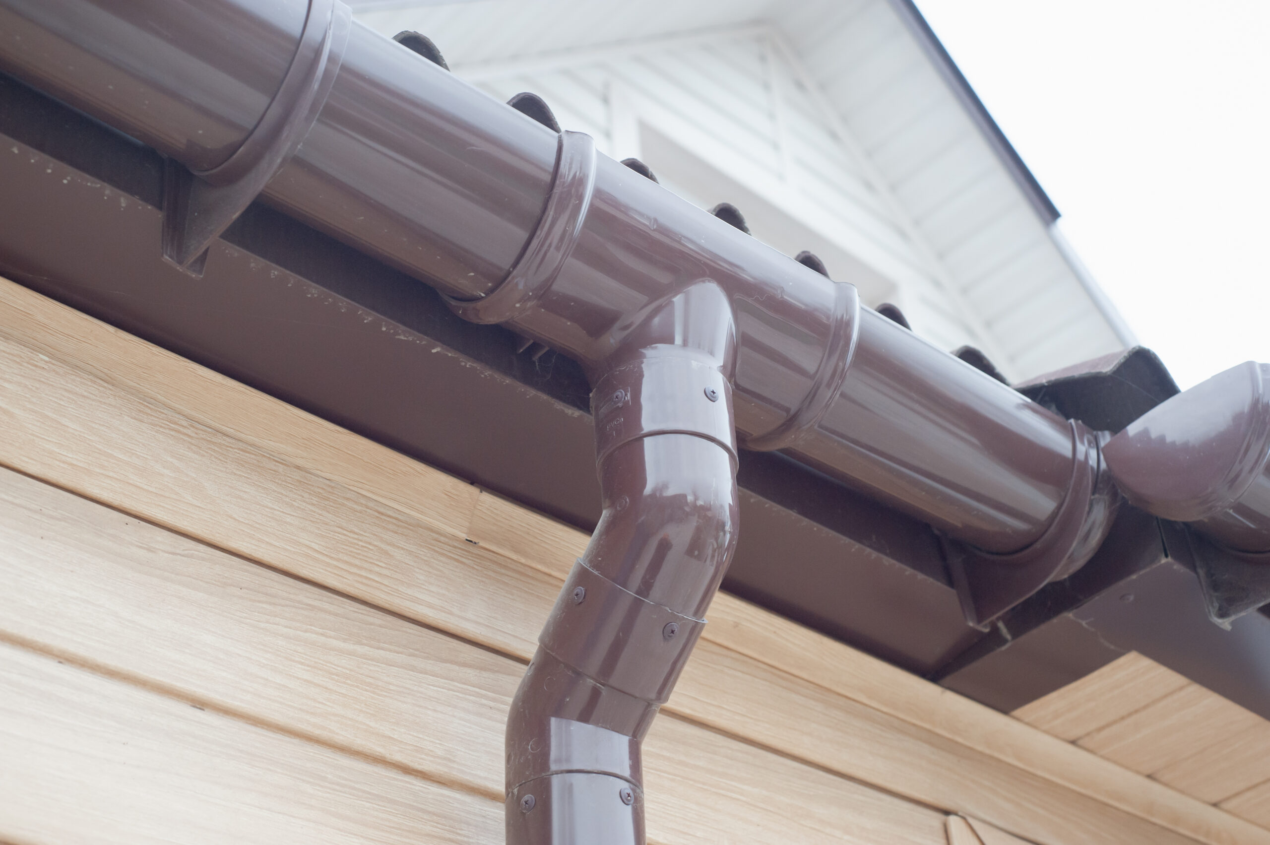 An angled view of new brown round gutters with a downspout attached.