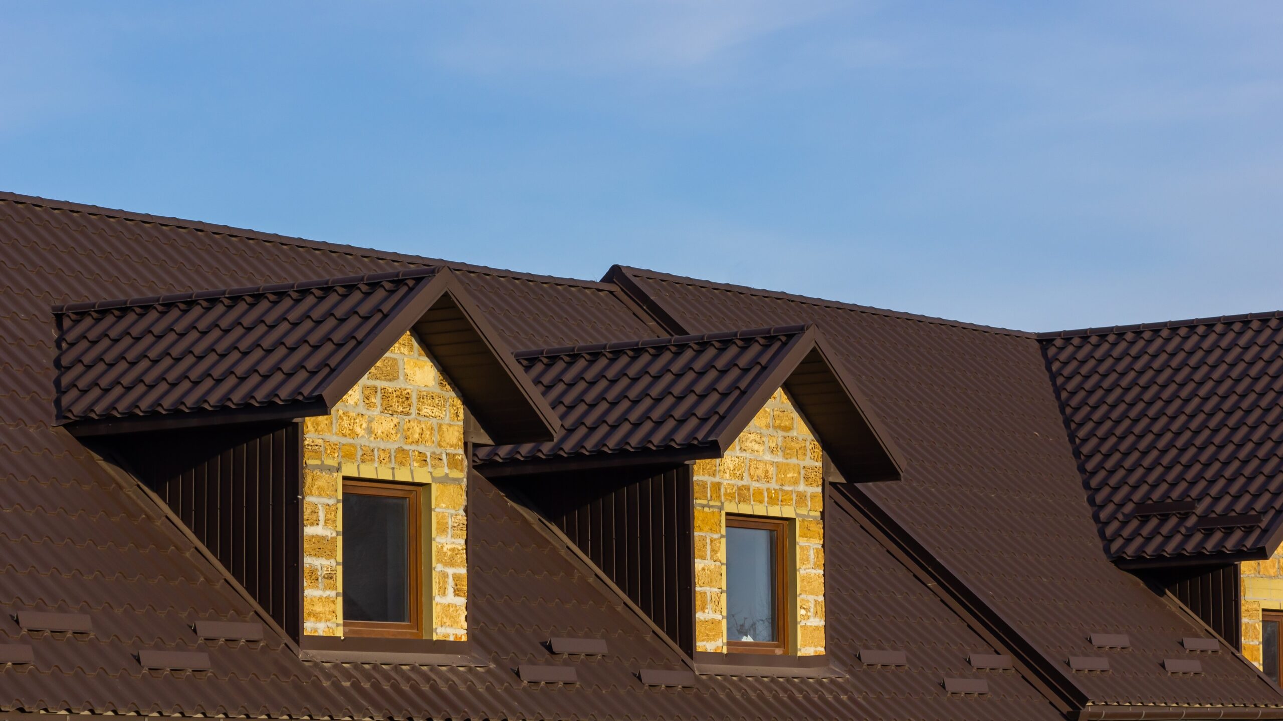 Dark red metal roof on home with a yellow brick facade.