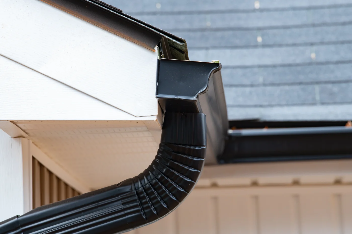 A black seamless gutter with a downpipe on the edge of a home.
