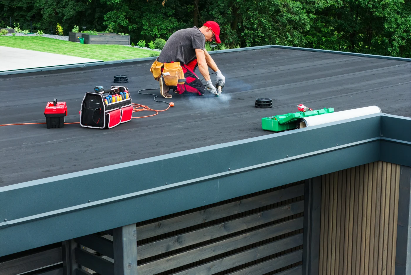 A roofer is on top of a home sealing the flat roof.